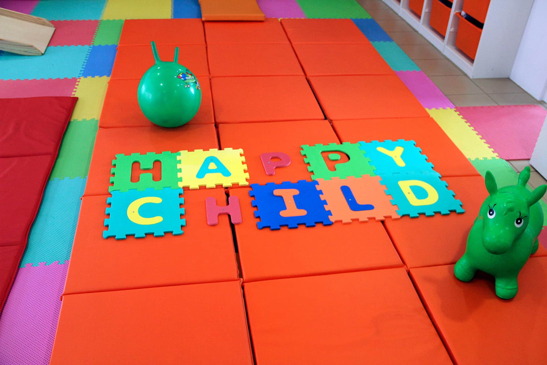 Tapetes coloridos no chão, puzzle de letras e brinquedos no Centro Happy Child.